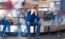 Uomo seduto sul rullo dei bagagli in aeroporto tiene le mani sulla testa
