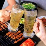 persone che brindano con due boccali di birra e sul tavolo degli spiedini di carne