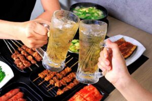 persone che brindano con due boccali di birra e sul tavolo degli spiedini di carne
