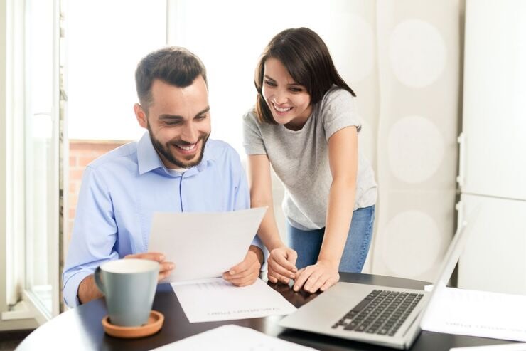 Uomo e donna leggono su foglio di carta entusiasti. Scrivania con PC, tazza