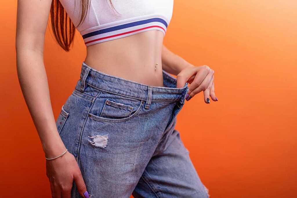 ragazza di profilo che con una mano si tira i jeans larghi