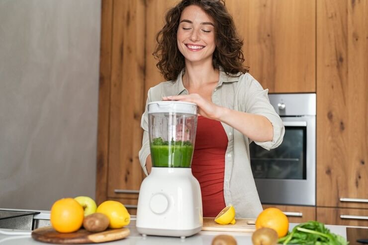 Ragazza felice aziona il frullatore con composto verde al suo interno