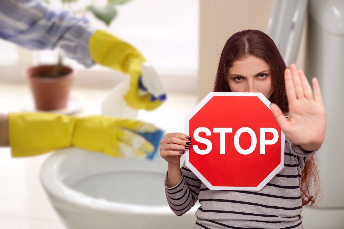 donna che pulisce wc e un'altra con cartello stop in mano