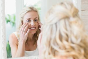donna davanti allo specchio che si tocca il viso con le mani
