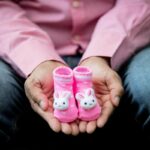 uomo con un paio di scarpine rosa da neonato in mano