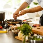 Uomo che versa qualcosa in padella, vari ingredienti sul piano da lavoro