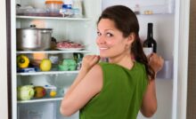 Ragazza con frigo aperto pieno guarda sorridente verso l'esterno