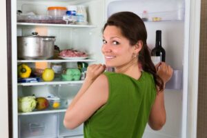 Ragazza con frigo aperto pieno guarda sorridente verso l'esterno