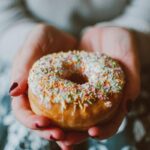 donna con in mano una ciambellina dolce ricoperta di zuccherini
