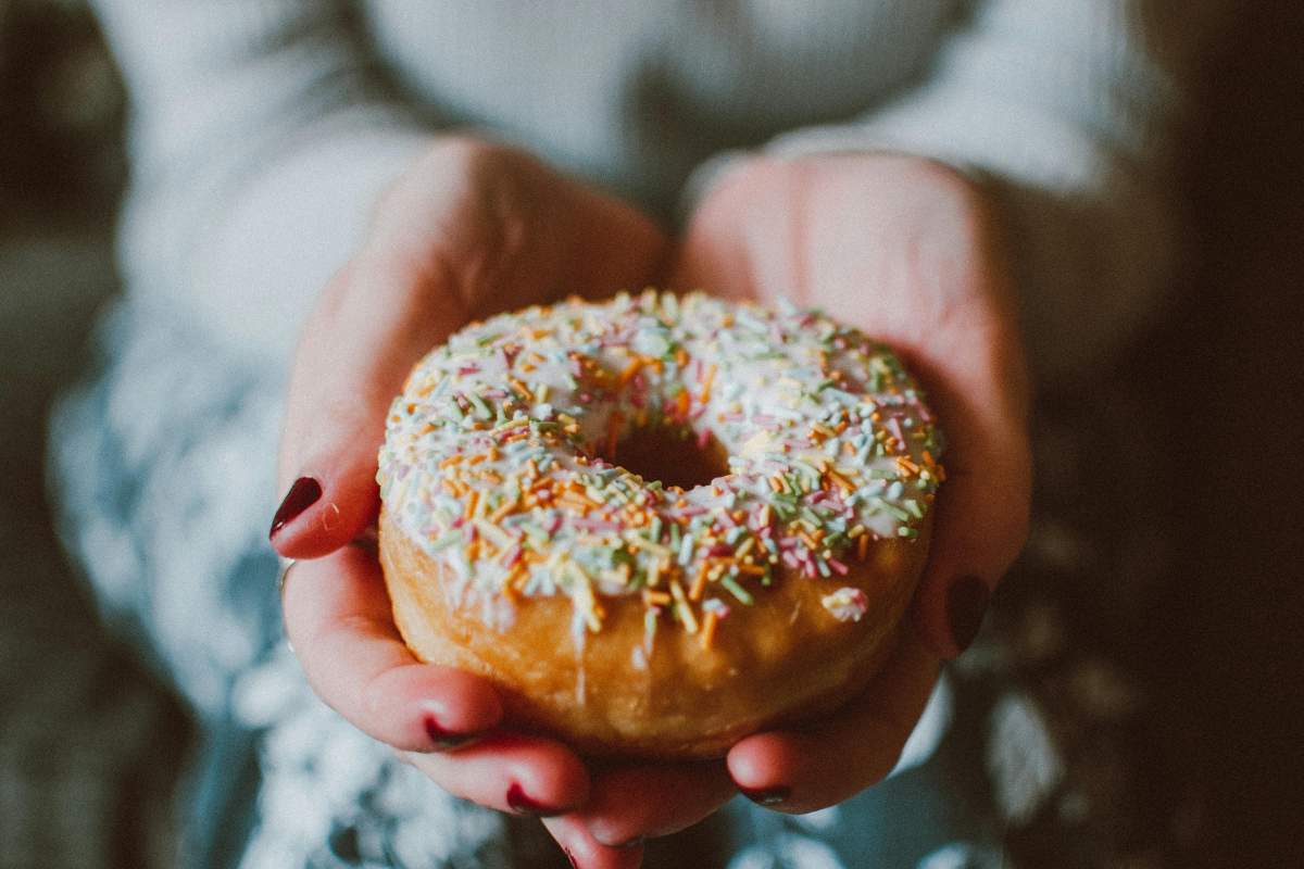 donna con in mano una ciambellina dolce ricoperta di zuccherini